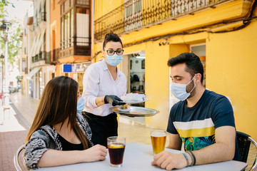 Waitress from a bar in Spain serves food and drinks to customers on her terrace. Everyone wears a mask to protect themselves from contagion. Phase one of the de-escalation. Social distance