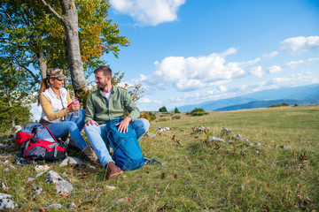 Young couple drinking water while resting on the rock during the travel in the mountains