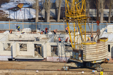 Photos of high-rise construction cranes and an unfinished house against a blue sky. Top view of the construction site.