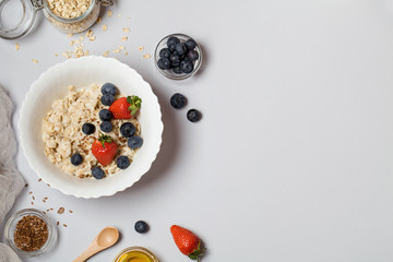 Oatmeal porridge with strawberry, blueberry, flax seeds and honey on gray background.