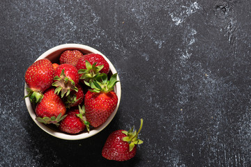Raw organic strawberries in the bowl on black rustic background with copy space for your design. Farmer’s market background.