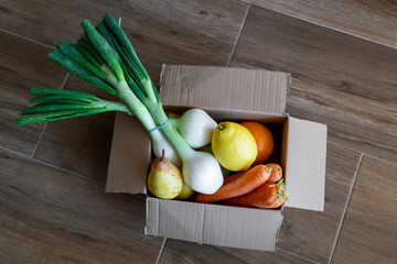 Fresh vegetables in cardboard box on brown wood background.