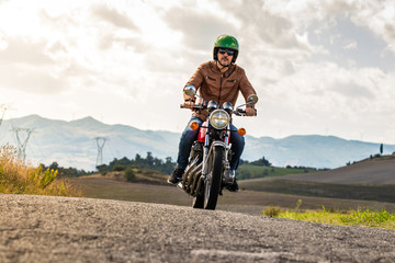 Obraz premium Man riding motorbike along a country road on tuscan hills landscape at sunset. Tuscany, Italy.