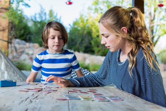 teen sister playing memory game on outdoor table with her 6 year old brother