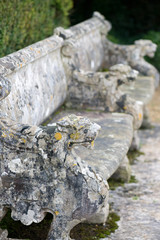 close up of a stone garden bench with a carved animal head armrest 