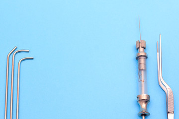 vintage syringe for intrauterine infusions and tonsillectomy on a blue background. a pair of medical tweezers and a syringe are next to it. copyspace