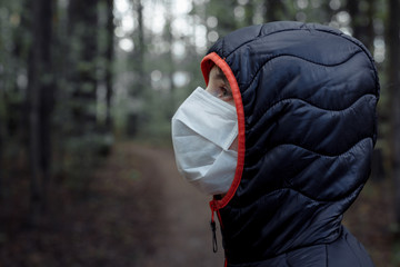 portrait of a girl in a medical mask and hood, who walks in the woods. concept of wearing a medical mask during a virus epidemic