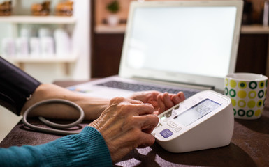 Fototapeta premium telemedicine concept elderly woman in an online consultation on video call from her kitchen taking her blood pressure
