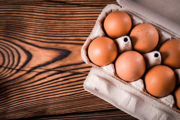 Detail close-up of chicken eggs in egg box on the old brown wooden background.