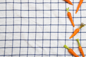Baby carrots over white table cloth with blue grid pattern. Flat lay, top view, creative layout with copy space.