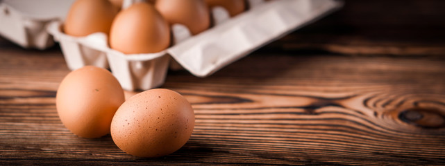 Banner detail close-up of chicken eggs in egg box on the old brown wooden background.