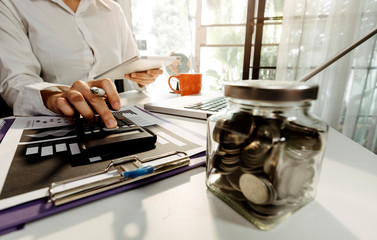 Businessman hands working with finances about cost and calculator and laptop with tablet, smartphone at office in morning light