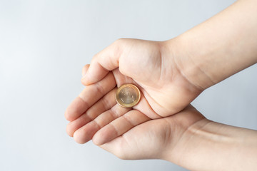 Finance crisis after coronavirus COVID19. Closeup child's hands holding One Euro coin isolated on white background, human hands and saving money concept.