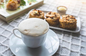 Home made cup of latte coffee beans with blurry cheese scones and summer book on coffee table with...