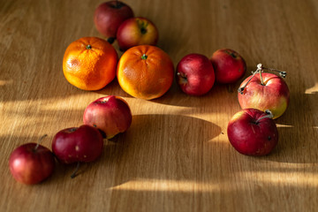 Naklejka na ściany i meble Bright juicy fruits, natural and natural fruits with damage. Red apples and tangerines on a modern brown light table