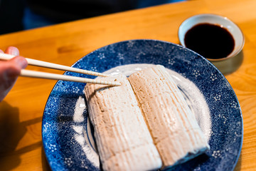 Closeup of hand holding chopsticks cutting Japanese traditional komo tofu dofu with soy sauce on...