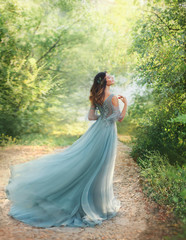 fairy tale princess in light summer blue, turquoise dress standing in park. Happy Woman walks...