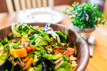 Closeup of fresh green mixed lettuce salad in bowl plate with bell peppers in rustic dining room wooden table and natural light