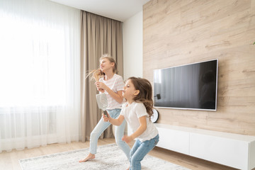 Two sisters having fun dancing in living room and singing karaoke, happy family concept