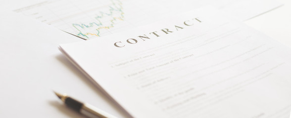 Contract paper and pen on white desk background. Focus on title Contract. Defocused pencil.