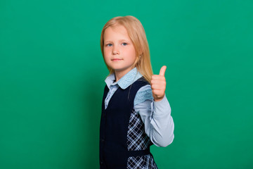 Little girl in school uniform shows thumb up gesture isolated on a green background.