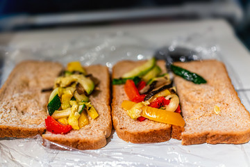Open plastic wrapped whole wheat grain bread closeup on airplane flight tray with crust and asian vegetable filling as vegan meal