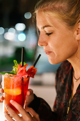 Blonde woman about to drink a red cocktail with a straw at night