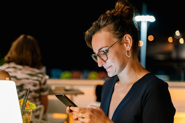 Profile of a woman with glasses using her mobile phone on a terrace at night