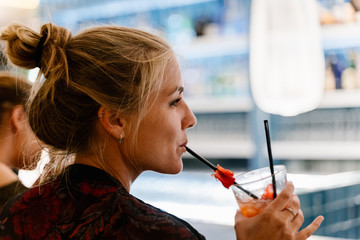 Profile of a blonde woman on her back drinking a cocktail and sitting at a bar