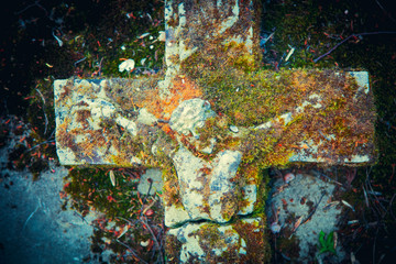 The crucifixion of Jesus Christ against gray stone slab. Fragment of very old stone partially destroyed statue in moss.