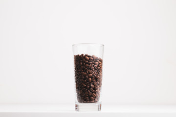 Roasted coffee beans in a big glass on white background. 