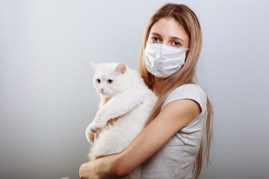 Woman in protective surgical mask holds cat pet in face mask. Chinese Coronavirus disease COVID-19 is dangerous for pets