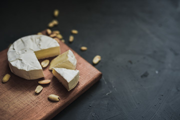 Camembert round cheese and a slice lie on a wooden board. grey matte concrete background. peanut
