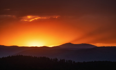 Fototapeta premium Sun setting over hills. Red clouds
