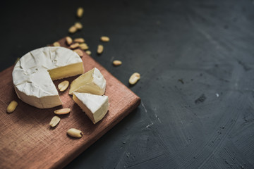 Camembert round cheese and a slice lie on a wooden board. grey matte concrete background. peanut