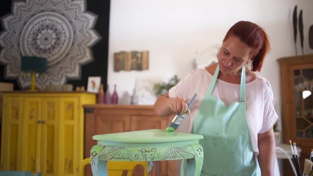 Mature craftswoman painting antique furniture while adding finishing touches