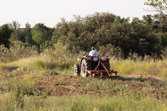 Agricultor en tractor rojo arando la tierra en el campo para sembrar un cultivo de cereales