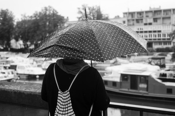 Portrait of woman standing in the street with black umbrella on back view