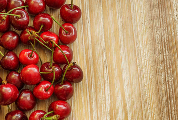 Still life with group of red cherries placed on the left side of the image on a light-toned wooden table with rustic texture.