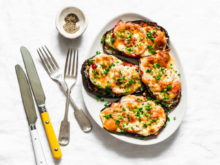 Baked aubergine with ham, tomatoes and mozzarella cheese - delicious appetizer, tapas on a light background, top view