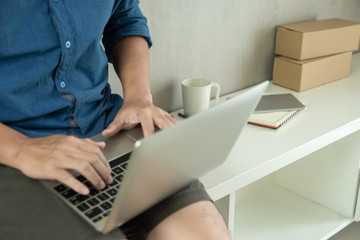 A man in a blue shirt is sitting using a laptop to work with coffee on the white sofa. A man who watches social media. .