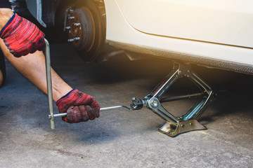 Hand using car jack for lifting tire emergency change and maintenance service.