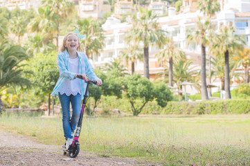 Active little toddler girl riding scooter on road in park outdoors on summer day.  Summer time fun