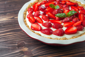 Strawberry cheesecake with basil leaves, in a red ceramic baking dish on a wooden background