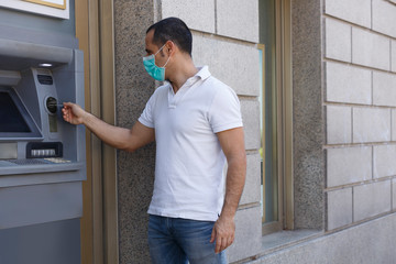 Fototapeta na wymiar Uomo moro con polo bianca preleva dei soldi dal bancomat di una banca fronte strada grazie alla sua carta di credito