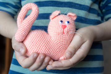 The child holds a toy knitted from the yarn of a pink cat. The child holds a toy in his hands.