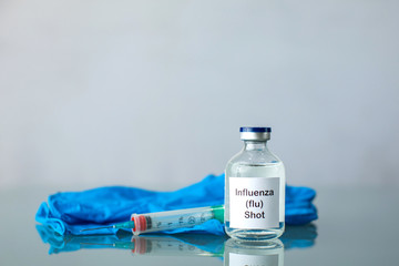 A bottle of a clear medicine influenza flu vaccine along with a syringe and surgical gloves with copy space
