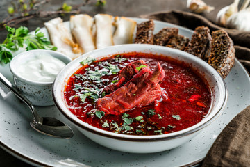 Ukrainian and Russian traditional beetroot soup - borscht in bowl with rib eye meat, rye bread, slices of bacon and sour cream on wooden background. Healthy food, close up