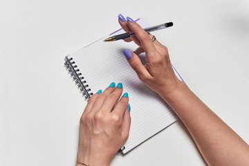 The girl thinks what to write in a notebook, holding a pen, a top view of the hand with a notebook and a pen. Personal diary, records, or business. Blank sheet to fill in