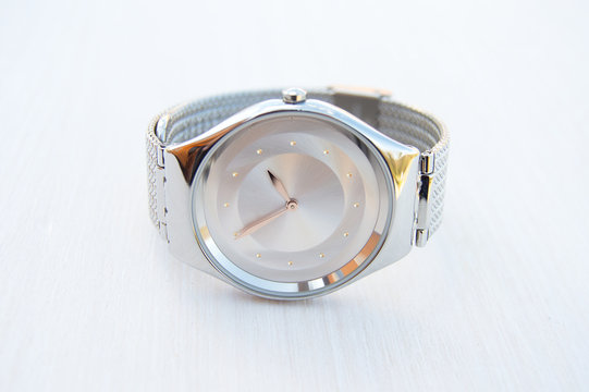 A fashionable women's wristwatch with an adjustable metal bracelet and a shimmering dial with a pale purple radial Polish. The clock stands on a white background.